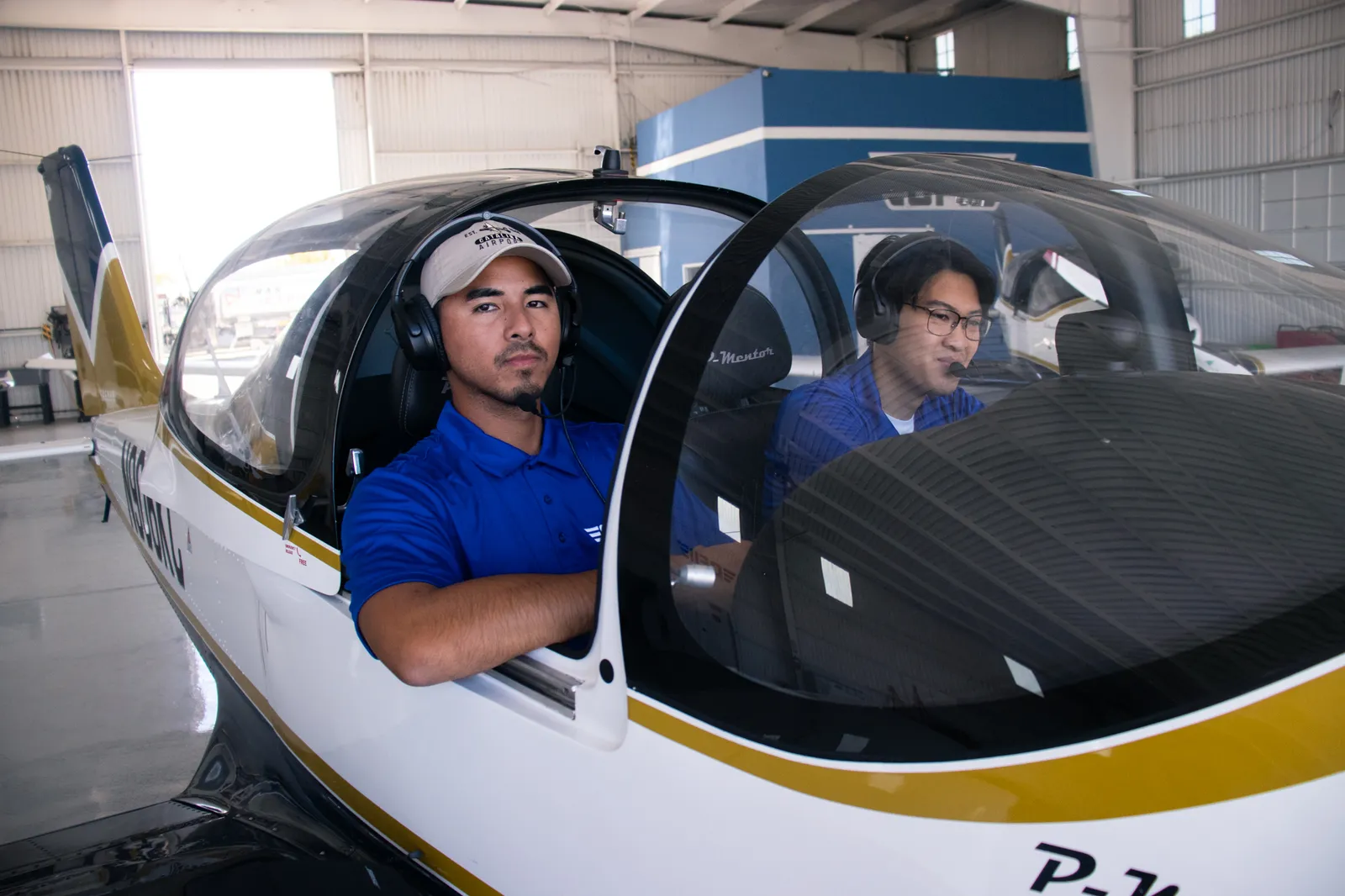 A student and an instructor in the cockpit of a P-Mentor in the hangar, headsets on, ready to taxi