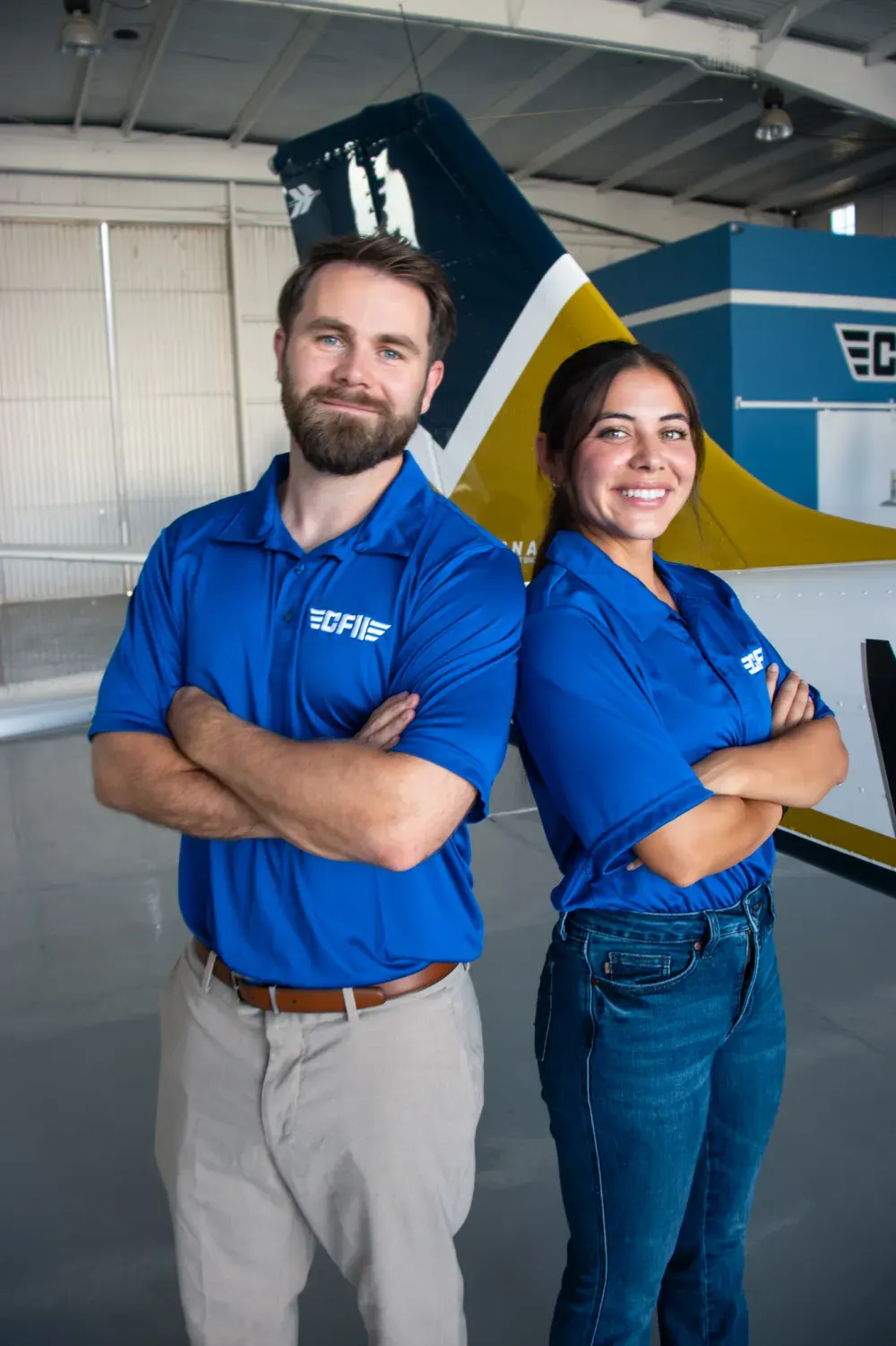 A CFII instructor and a student standing back to back in front of a P-Mentor in our hangar at Riverside Municipal Airport