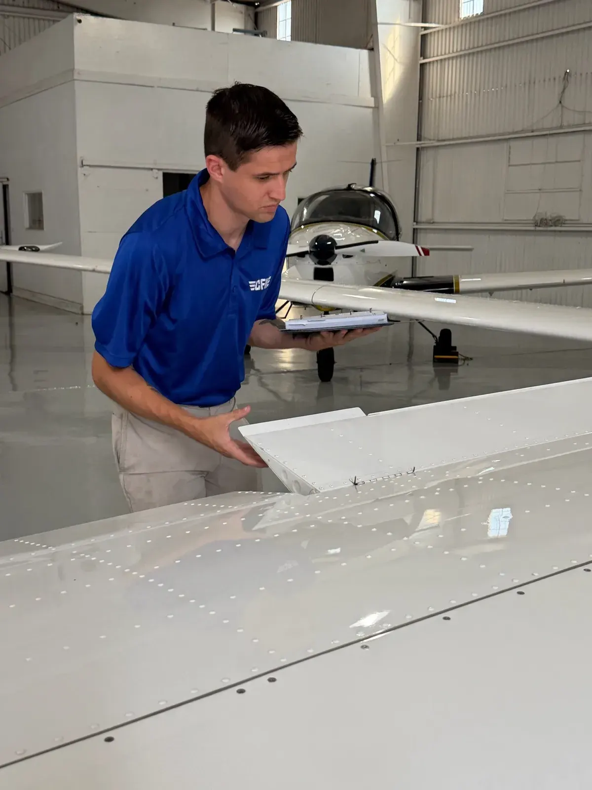 A student with a checklist doing a preflight inspection of a P-Mentor wing in the hangar