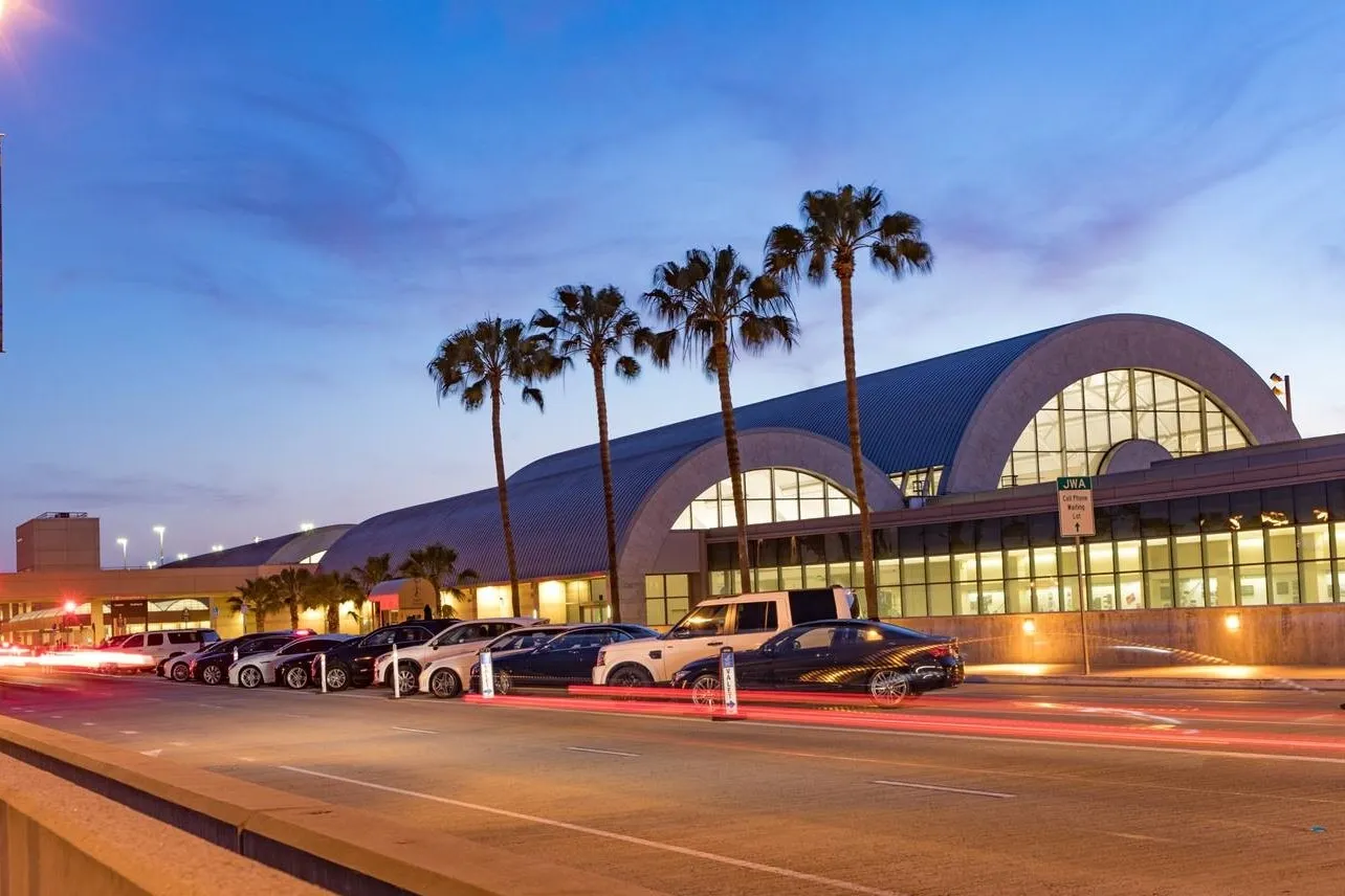 The Thomas F. Riley Terminal at John Wayne Airport at dusk, with its arched roofs and a row of palm trees along the curb