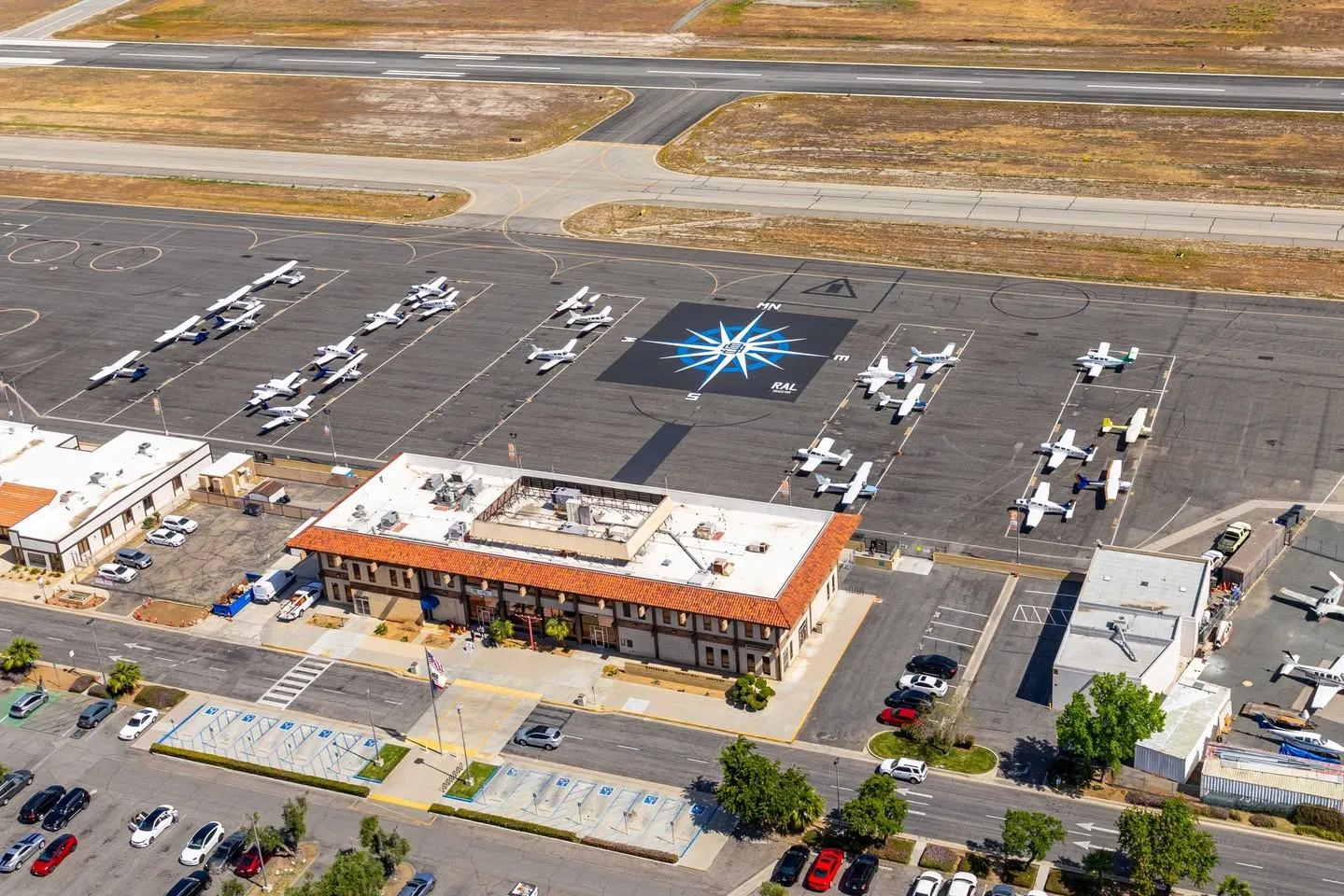 Aerial view of Riverside Municipal Airport (KRAL): the terminal, the RAL compass rose on the ramp, parked airplanes and the runway